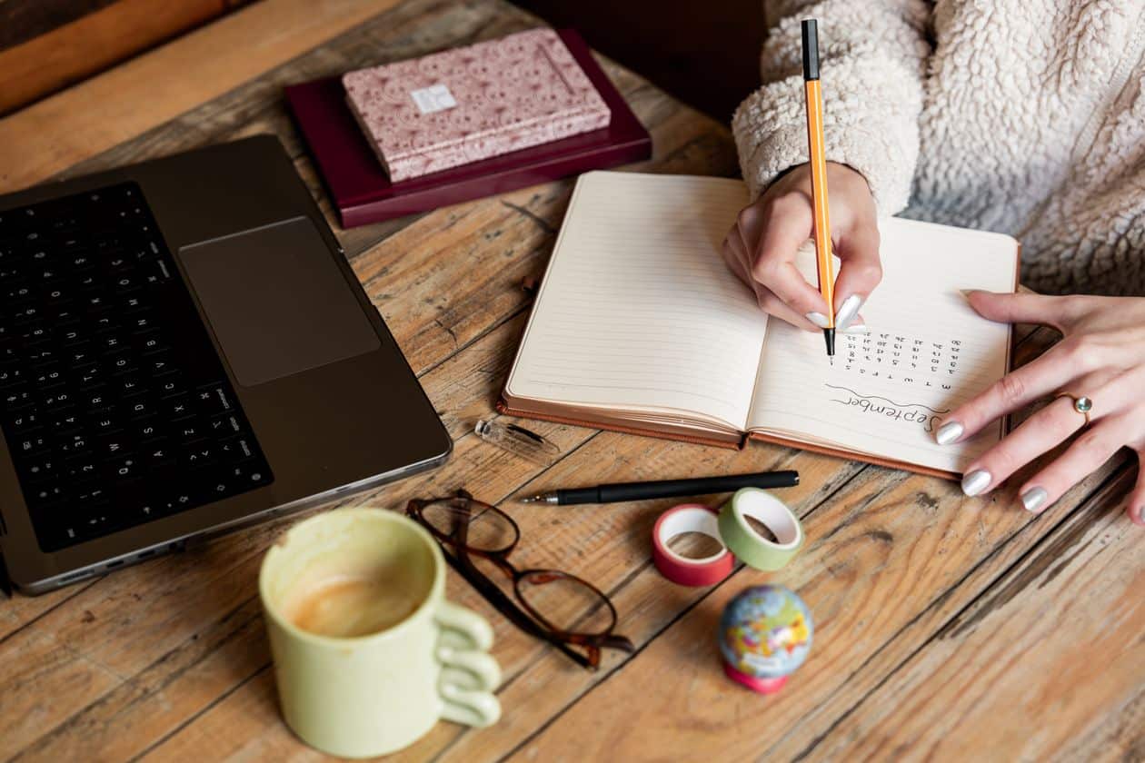 Woman writing in a notebook at her desk while budgeting