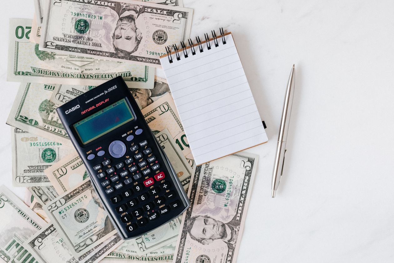 Calculator and notepad placed over a stack of paper bills