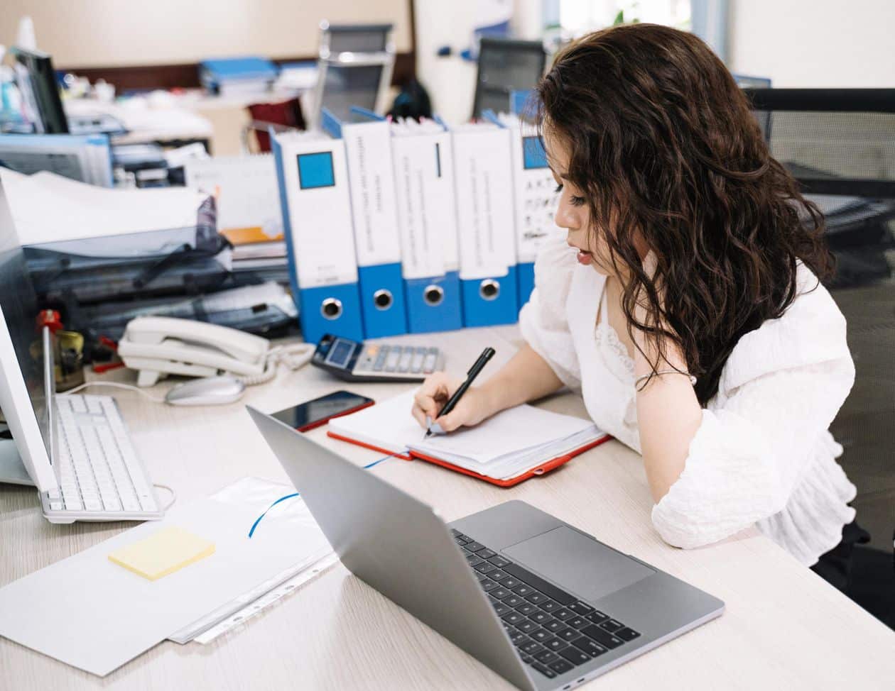 Woman writing in a notebook next to her laptop, working as a freelance writer from home
