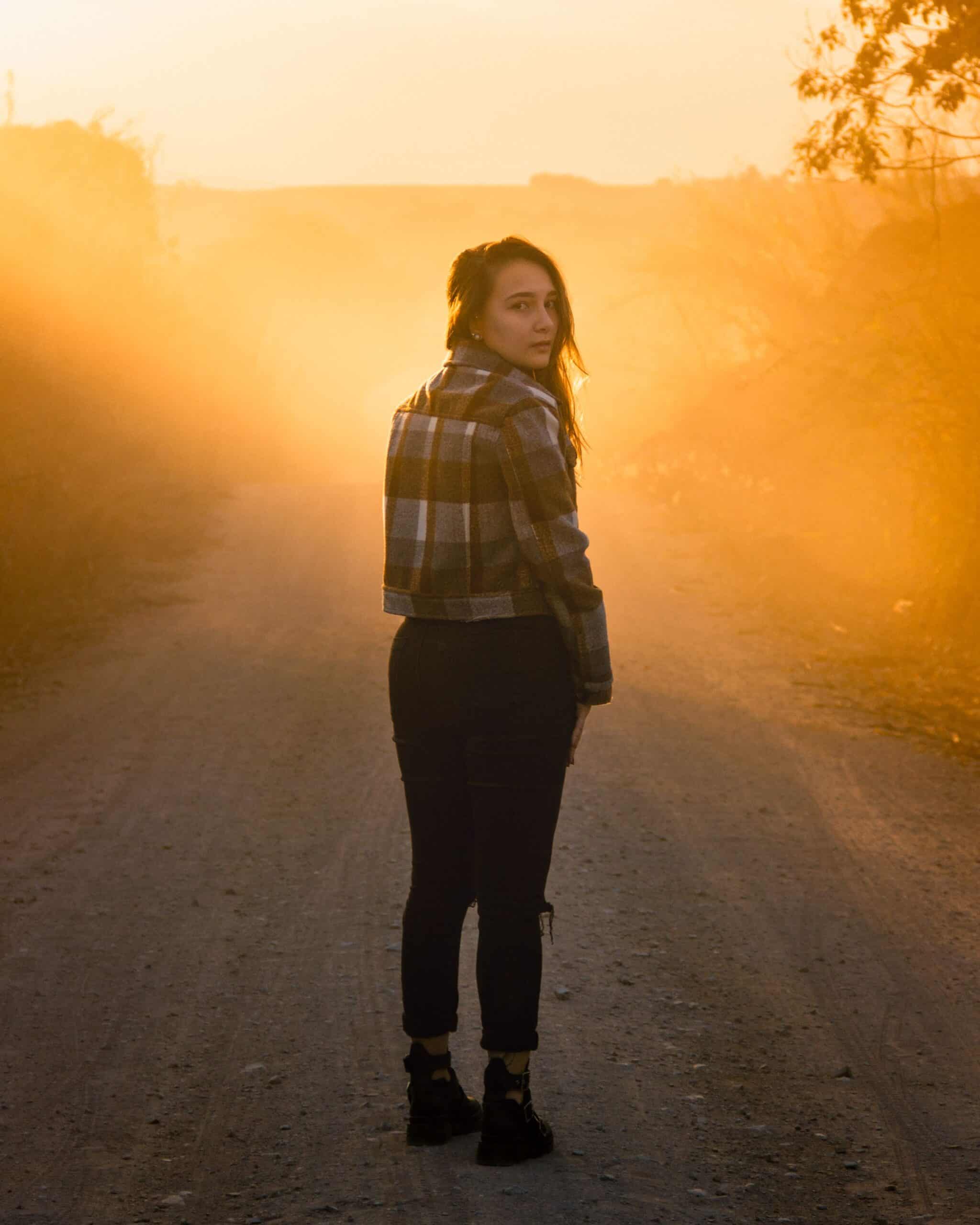 Woman standing on a quiet road at sunrise, looking ahead with confidence