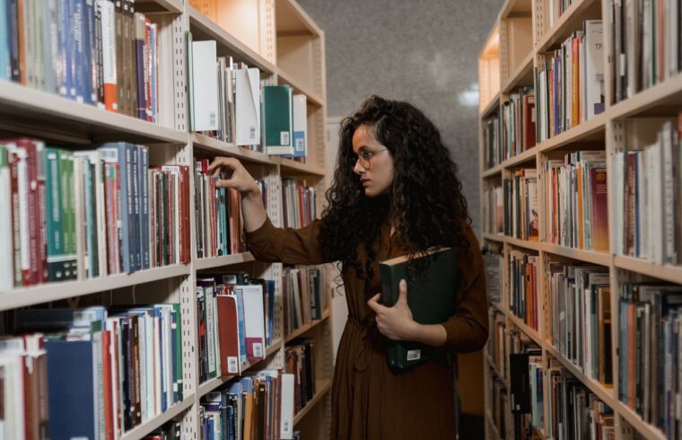 Woman choosing a book on a shelf, comparing degree options for a career change at 40