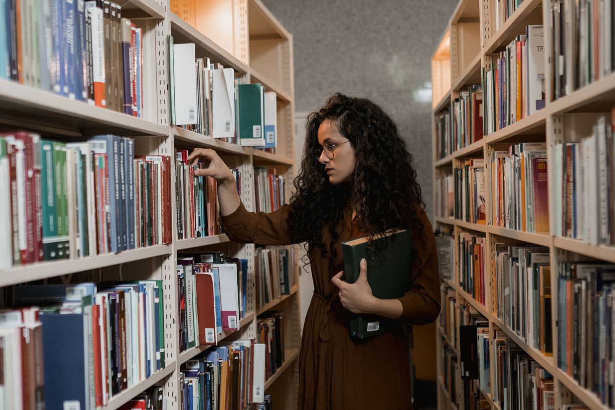 Woman choosing a book on a shelf, comparing degree options for a career change at 40