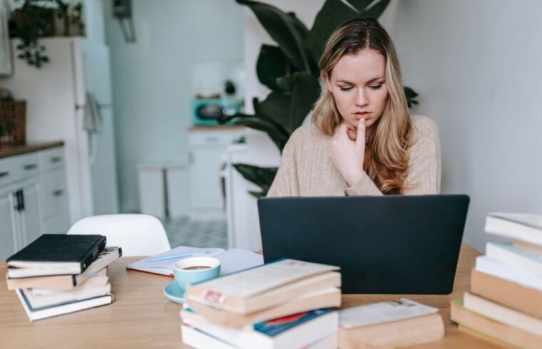 Adult student researching online degree programs with a laptop and books spread on the table