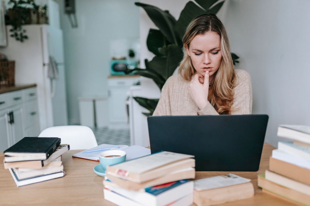 Adult student researching online degree programs with a laptop and books spread on the table