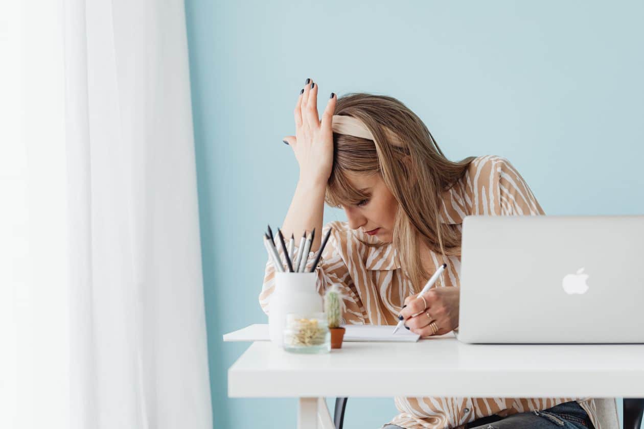 Woman writing on a notebook near her laptop while working on freelance projects
