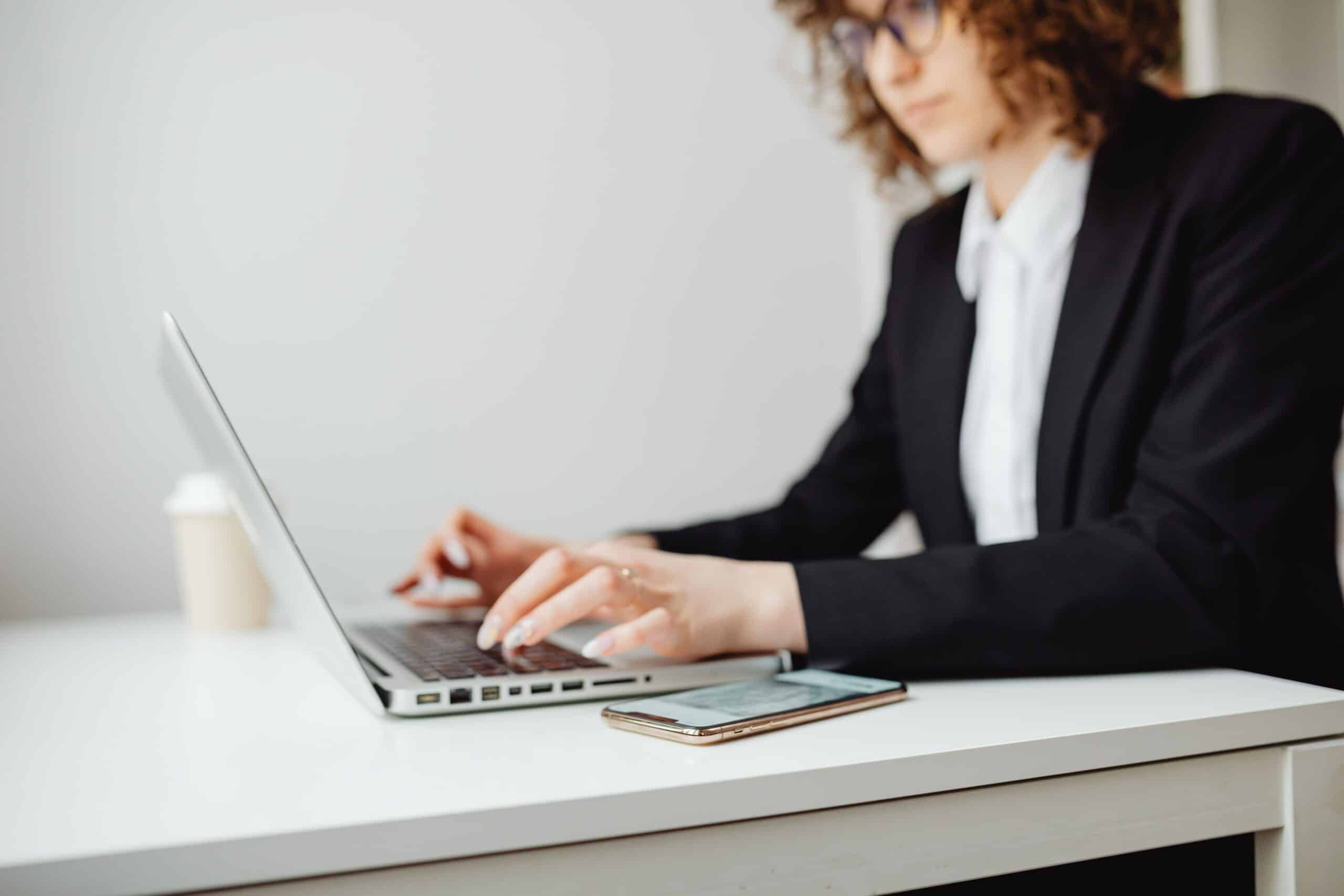 Woman in a blazer typing on a laptop, editing her resume