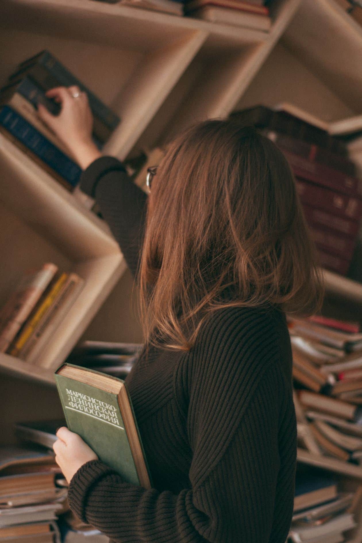 Woman picking a book from a bookshelf, weighing which degrees deserve more caution